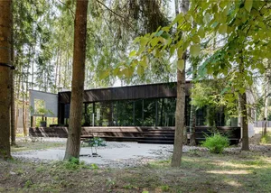A modern house exterior made of wood, surrounded by trees.
