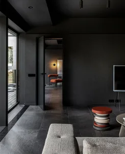 A modern living room with dark walls, concrete flooring, and metal furniture. A floor lamp is illuminating the space, and a t