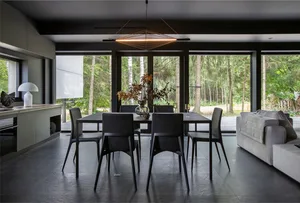 Modern minimalist dining room featuring black metal table and chairs with large windows showcasing natural forest view.