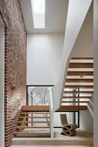 A modern staircase with wooden steps and a brick wall, featuring a glass window and a contemporary chair.