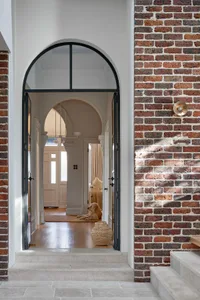 Architectural entryway with brick walls and wooden flooring, featuring a dog sitting on a rug.