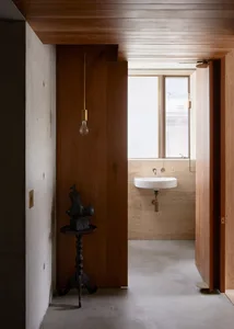 A modern minimalist bathroom with concrete walls and floor, featuring a wall-mounted sink and a hanging light bulb.
