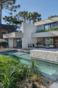 Modern residential home with outdoor swimming pool, concrete patio, glass doors, and stone accents.