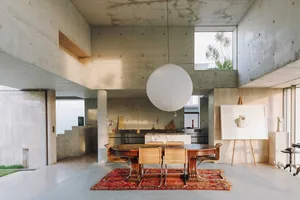 Concrete living room with modern design, featuring exposed concrete walls, a dining table with wicker chairs, and a large sph