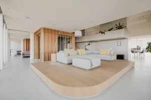 Modern living room with a large sectional sofa in a light-colored fabric, a curved floor lamp, and a raised platform.