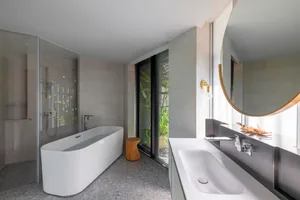 A modern minimalist bathroom featuring a white freestanding bathtub, a large sink area, and a glass shower enclosure, with co
