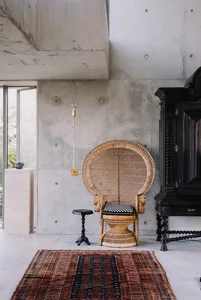 Industrial-style living room featuring a concrete wall, a rattan armchair, and a wooden stool.