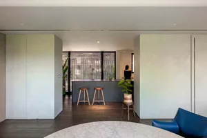 A minimalist kitchen with a concrete backsplash, featuring a bar counter with stools and a potted plant.