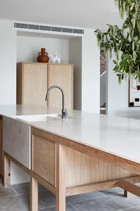 Modern minimalist kitchen with white marble countertops and wooden cabinetry.
