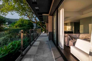Modern residential balcony with concrete flooring and a view of the greenery, featuring a living room with sofas and a large