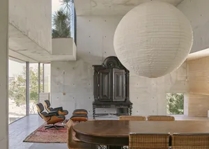 A modern living room with concrete walls, a large spherical pendant light, and minimalist furniture.
