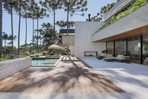 Modern house with a concrete exterior, featuring a swimming pool and outdoor lounge area surrounded by tall trees.
