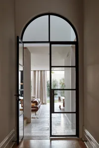 Modern entryway with glass and metal doors and a view into a living room with a sofa and coffee table.
