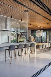 A modern kitchen with a concrete countertop, stainless steel appliances, and high-back upholstered bar stools.