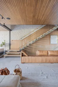 Modern living room with a wooden ceiling, beige sofa, and glass stairway.