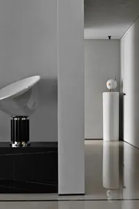 A minimalist interior featuring a white, ribbed concrete column and a black and white modern lamp.