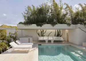 Modern living area with concrete walls and floor, featuring comfortable seating and a serene outdoor pool with greenery.