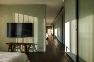 Modern, minimalist interior with concrete finishes, a white bed, and a wooden bench in front of a wall-mounted television.