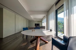 Modern minimalist dining area with marble tabletop and wooden furniture, featuring a wooden floor and glass windows.
