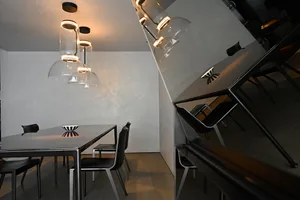 A modern minimalist restaurant interior with metallic tables and chairs, white walls, and clear pendant lights.