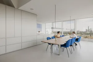 Two people sitting at a wood dining table in a modern residential interior with white walls and blue fabric chairs