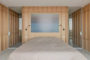 A minimalist bedroom with wood paneled walls and a gray bedspread.
