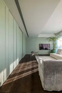 Modern minimalist living room featuring a wooden floor, white furniture, and a large potted plant.