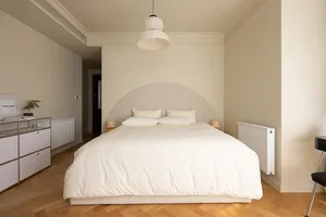 A minimalist bedroom with a bed dressed in neutral-colored bedding and a curved headboard.