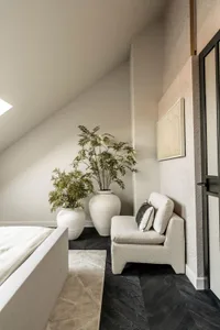 Minimalist bedroom with black hardwood floors, wooden patterns on walls, minimalist white furniture, green potted plants, and