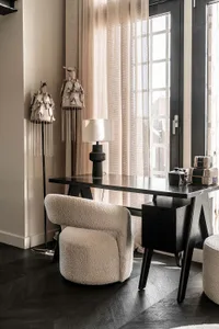 A minimalistic home office featuring a black wooden desk, a white blanket, and curtains by the window.