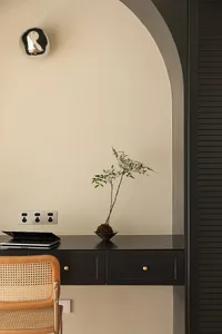 A minimalist workspace featuring a black desk with a small plant, a wooden rattan chair, and a laptop.