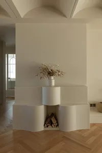A minimalist white living room with a vase of dried flowers and firewood storage.