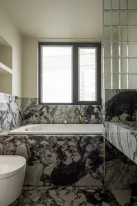 Modern bathroom with white marble fixtures and black accents, featuring a freestanding bathtub and a window with blinds.