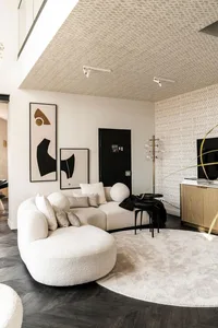 Modern living room featuring a comfortable white sectional sofa with round ottoman, geometric wall art, and a round rug in a