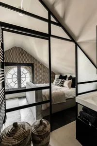A minimalist bedroom with a simple bed, geometric wallpaper, and textured textiles in beige and black