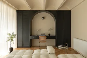 A minimalist home office featuring a sleek black desk with a white cushioned bench and a small potted plant.