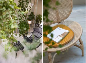 A minimalist living space featuring a wicker chair with a cushion and a coffee table, surrounded by greenery.