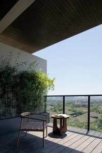 A modern balcony featuring a wooden chair, glass table, and greenery.
