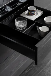 An open kitchen drawer showing black wooden compartments for dishes and cups.