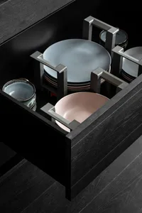 Close-up of modern black kitchen storage with metal organizers and ceramic plates and bowls.