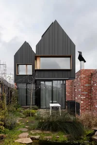 A stylish, modern house exterior with black metal cladding, large windows, and a brick wall.
