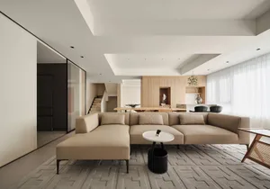 Modern minimalist living room featuring a beige sectional sofa, white coffee table, and light wood elements.