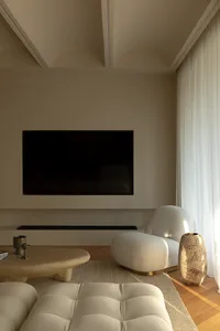 A modern living room with a neutral color palette featuring a TV on the wall, white furniture, and wooden floor.