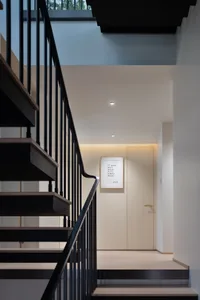 Modern staircase with black handrail and wooden steps against a white wall.
