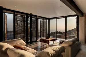 A modern, minimalist living room with concrete surfaces, natural light, and ocean views.