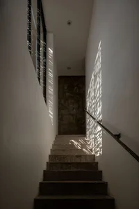 Minimalist staircase with concrete steps, glass barrier, and shadows on the wall.