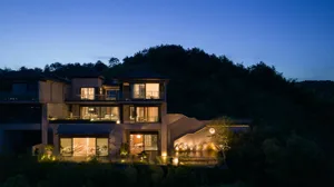 A modern residential house with concrete exterior cladding at dusk with illuminated windows.