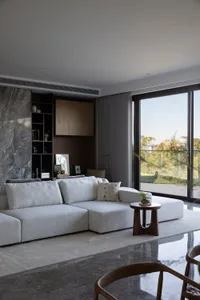 Modern living room with a white sectional sofa, marble fireplace, and large windows.