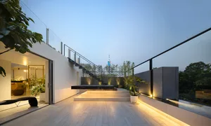 A modern rooftop garden extension with wooden floors, concrete walls, and glass railings illuminated by warm lighting.