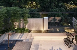 A modern rooftop garden with natural stone furniture, surrounded by lush greenery and illuminated by warm lights.